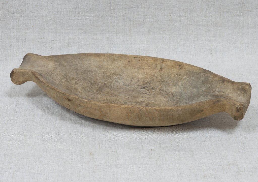 Деревянная овальная чаша с короткими ручками по двум сторонам, использовалась для подачи или перемещения пищи в быту. Поверхность гладкая, без украшений